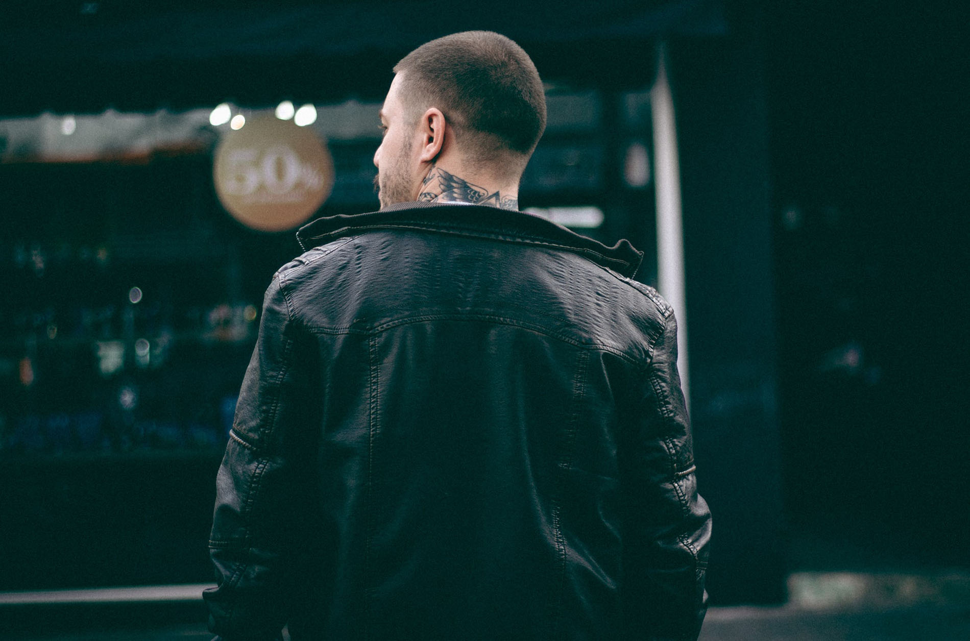 A man with a beard and tattoos wearing a black jacket.