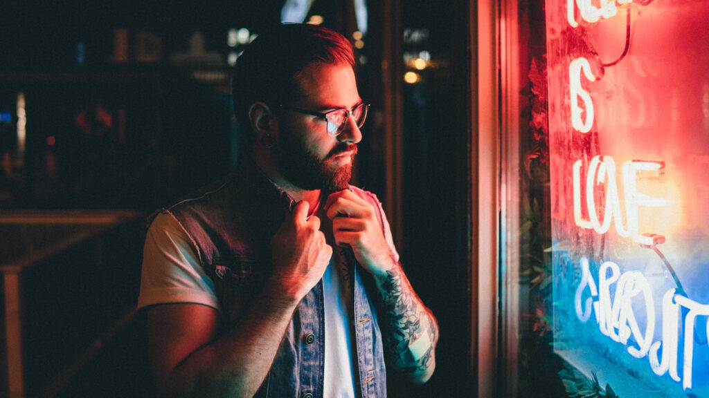 A man with glasses and beard tying his tie.