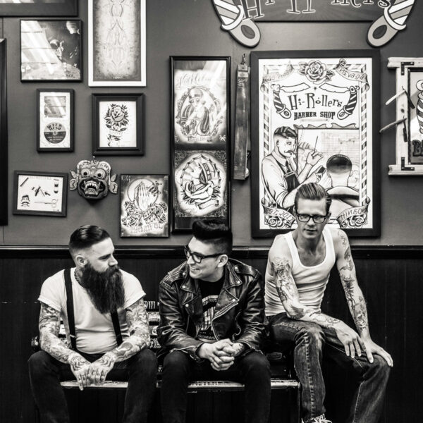 Three men sitting on a bench in front of some tattoos.