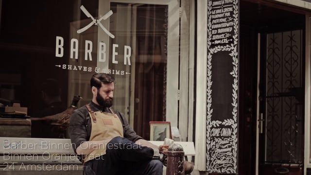 A man sitting on the ground outside of a barber shop.