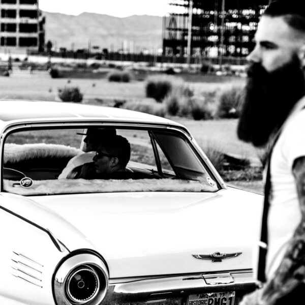 A man with a beard and mustache sitting in the passenger seat of an old car.