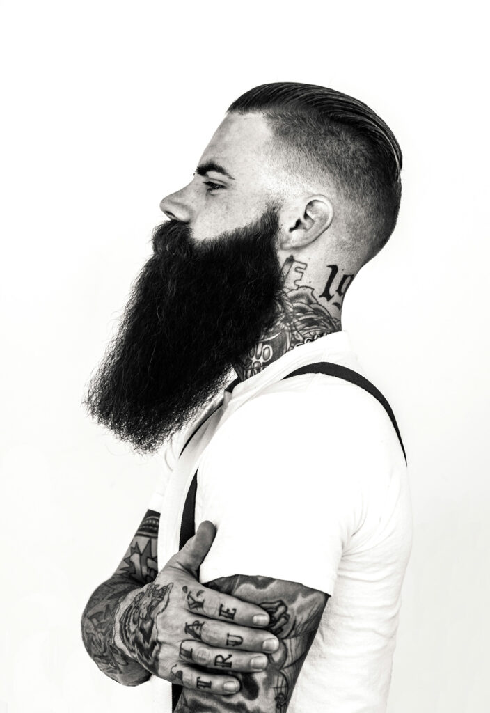 A man with a beard and mustache has a tattoo on his neck.