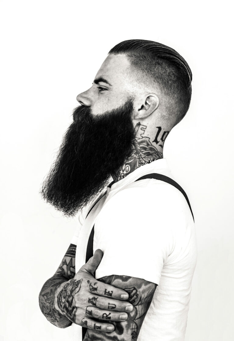 A man with a beard and mustache has a tattoo on his neck.