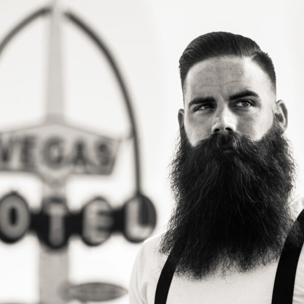 A man with long beard and mustache standing in front of an old vegas sign.