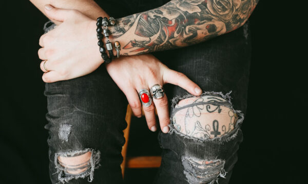 A person with tattoos and rings sitting on their lap.